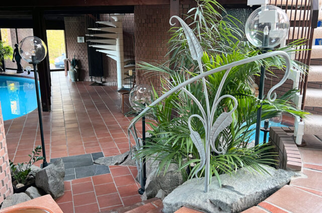 Forged leafy handrail fitted into large grey boulders by poolside.