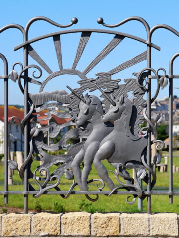 Forged and fabricated from mild steel, painted Ratho Grey. The panel shows a setting sun with sun rays, two prancing unicorns and textured metal strands representing water and landscape.