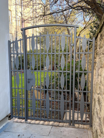 Fabiricated gate with side panels and arch. Lozenge shapes running down the upright bars riveted to the horizontal bars. Painted Ratho Grey.
